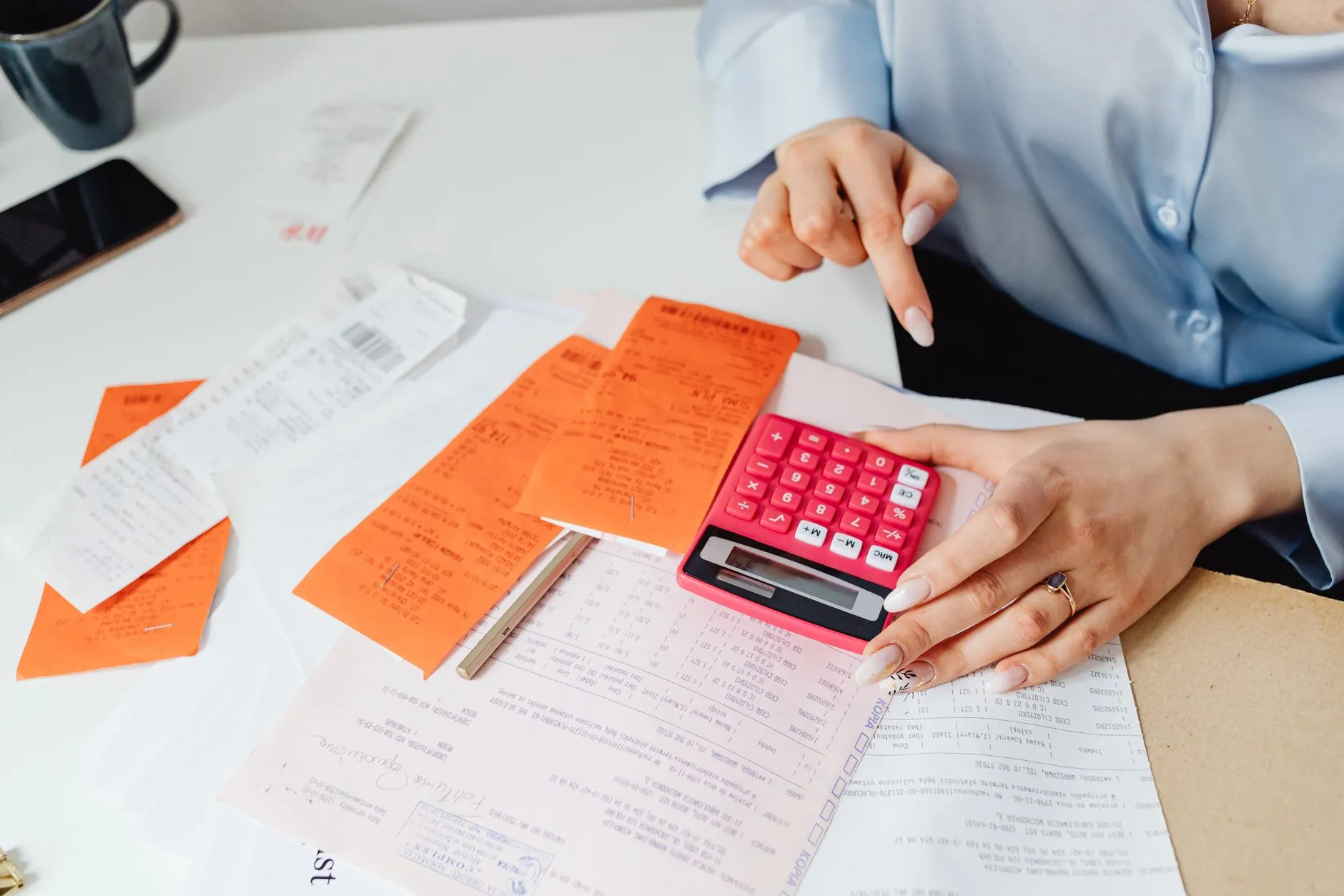 Mujer calculando gastos con tiques y una calculadora en su mesa