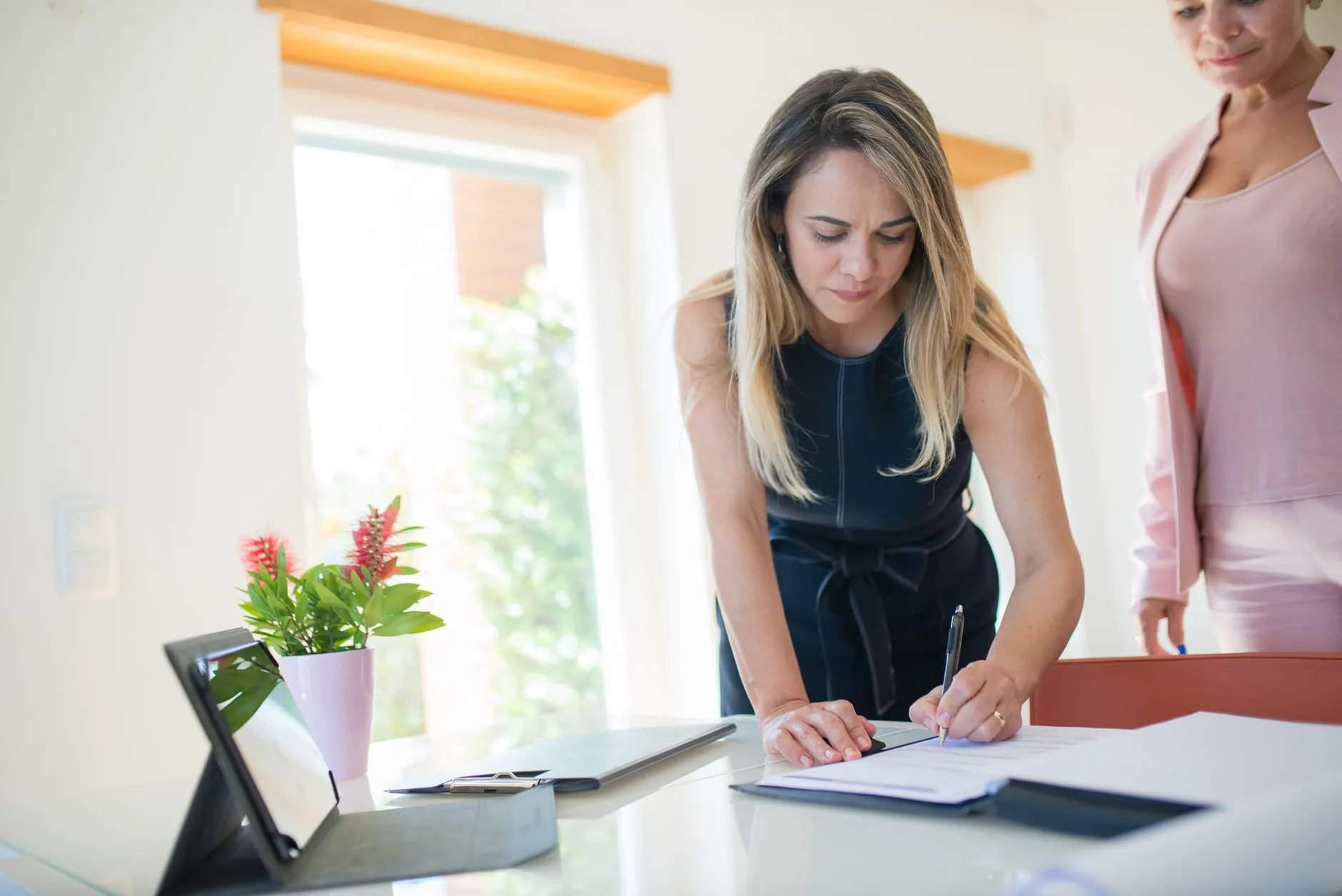 Empresaria firmando documentos en su oficina junto a una tableta